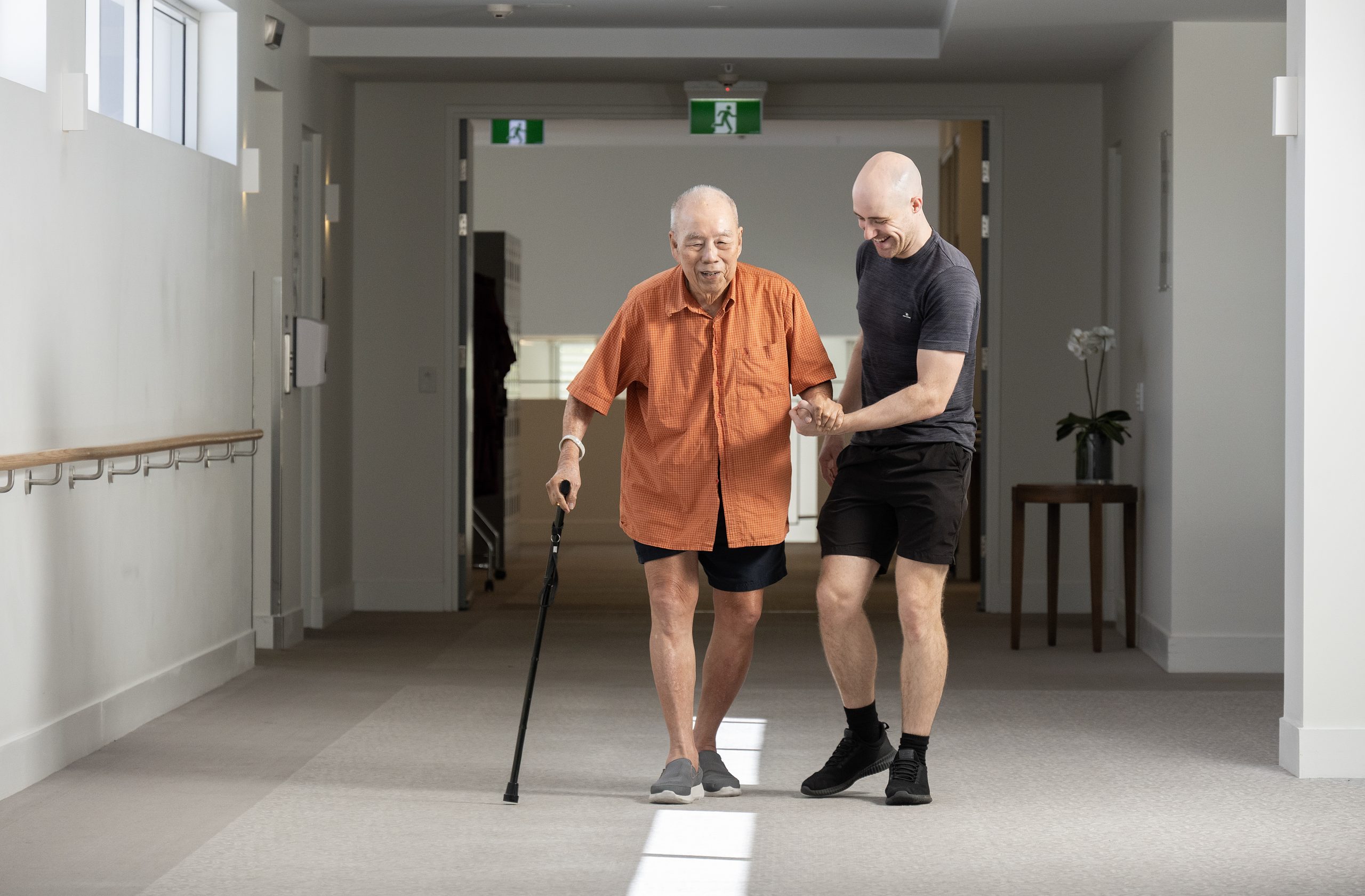 Mobile physiotherapist walking alongside an older man using a walking stick in Hollywell
